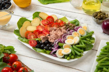Geleneksel Nicoise salatası beyaz dikdörtgen salata kasesinde eski beyaz bir masa üzerinde sos ve malzemelerle. Seçili odak. 