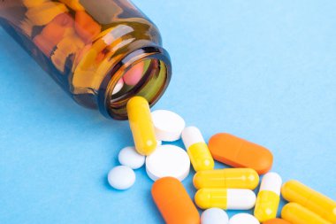 Mavi arkaplandaki cam şişeden çok renkli tabletler ve haplar.