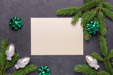 Noel tebrik kartı, köknar ağacı dalı, gümüş süsleme ve boş kağıt maketi. Karanlık taş arka plan. Üst Görünüm - Resim