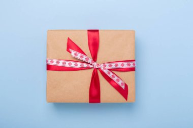 Mavi arka planda Noel hediyesi kutusu. El işi kâğıdı, kırmızı kurdele. Kopyalama alanı olan üst görünüm - Resim