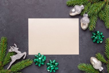 Noel tebrik kartı, köknar ağacı dalı, gümüş süsleme ve boş kağıt maketi. Karanlık taş arka plan. Üst görünüm