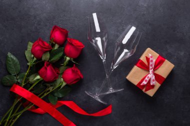 Red rose flowers bouquet, gift box, champagne glasses on black stone background Valentine's day greeting card Copy space Top view