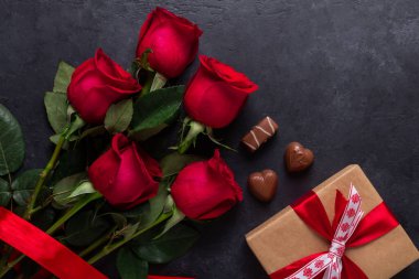 Kırmızı gül buketi, hediye kutusu, siyah taş zemin üzerinde çikolata tatlısı Sevgililer Günü tebrik kartı Kopya uzayı
