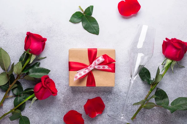 Kırmızı gül buketi, hediye kutusu, arka planda şampanya bardakları Sevgililer Günü tebrik kartı.