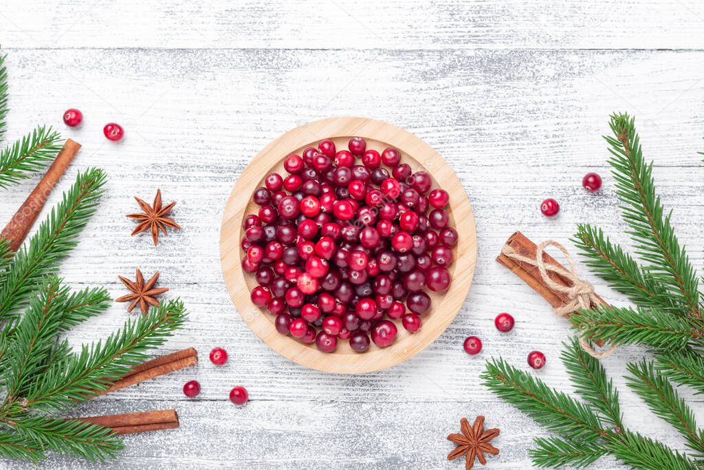 Raw fresh cranberries in wooden bowl, spice and fir branches on light wood background. Top view