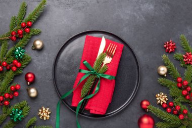 Siyah seramik tabağı, köknar ağacı dalı ve siyah taş zemin üzerinde kırmızı aksesuarlar olan Noel masası. Üst Manzara. Uzayı kopyala - Resim