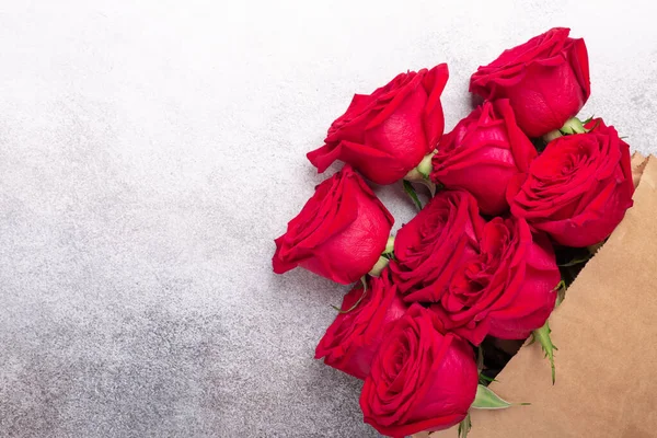 Craft paper shopping bag with flowers on stone background. Red roses in a brown kraft bag. Copy space - Image