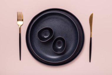 Pastel pembe arka planda siyah seramik tabaklar ve çatal bıçak takımı. Metnin için alanı kopyala - Resim