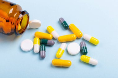 Mavi arka planda cam şişeden çıkan çok renkli tabletler ve haplar çeşitli ilaç tabletleri ve haplar. Sağlık hizmetleri, yakın çekim kopyalama alanı