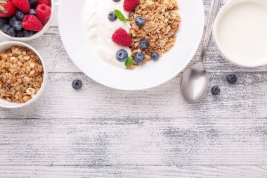 Yoğurtlu ev yapımı granola ve ahşap zemin üzerinde beyaz seramik tabakta taze böğürtlen.