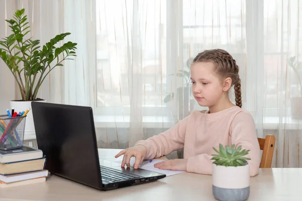 Шкільна дівчина сидить за столом і використовує ноутбук. Освіта вдома Назад до школи — стокове фото