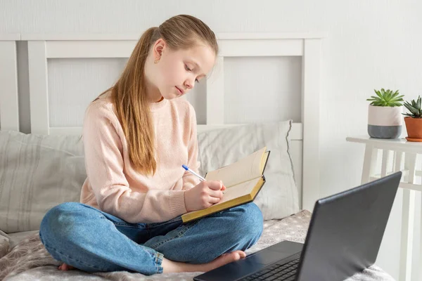 Дівчина-підліток робить домашнє завдання на ліжку вдома. Соціальна відстань, самоізоляція — стокове фото