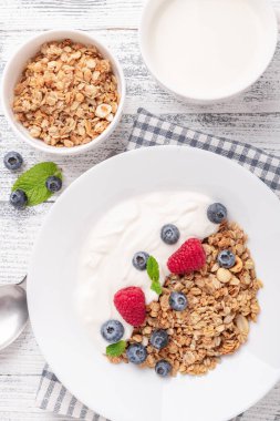 Yoğurtlu ev yapımı granola ve ahşap zemin üzerinde beyaz seramik tabakta taze böğürtlen. Dikey fotoğraf