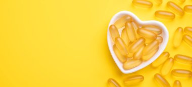 Omega 3 kapsülleri sarı arka planda kalp şeklinde bir plakada. Balık yağı softgelleri. D vitamini kapsülleri. Boşluğu kopyala