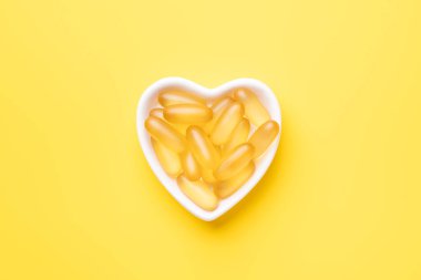 Omega 3 kapsülleri sarı arka planda kalp şeklinde bir plakada. Balık yağı softgelleri. Uzayı kopyala Üst görünüm