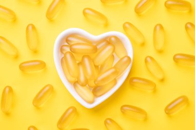 D vitamini ve Omega 3 balık yağı kapsülleri sarı arka planda kalp şeklinde bir tabakta. Sağlık hizmetleri kavramı. Üst görünüm