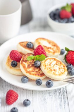 Taze dutlu süzme peynir krepleri, beyaz ahşap masada bir fincan kahve makinesi. Lezzetli kahvaltı yemekleri. Dikey fotoğraf