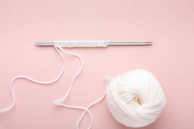 Beyaz örgü yünü ve pastel pembe arka planda örgü iğneleri. Kadın örgü hobisi. Üst görünüm