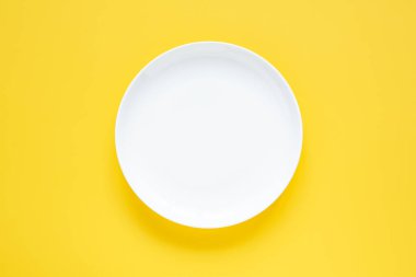 Sarı arkaplandaki boş beyaz seramik plaka Üst görünümü kopyala