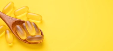 Omega 3 kapsüllerini sarı arka planda tahta kaşıkla kapat. Balık yağı softgelleri. Yatay pankart. Boşluğu kopyala