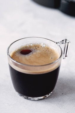 Şeffaf cam bardakta taze sıcak espresso. Taş zeminde sade kahve. Dikey