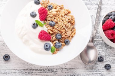 Fırında tahıllı yoğurt ve ahşap zemin üzerinde beyaz seramik tabakta böğürtlen. Sağlıklı kahvaltı. Boşluğu kopyala