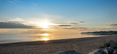 Onega Gölü 'nde gün batımı. Yansıması olan güzel bir manzara, mavi gökyüzü ve gün doğumunda sarı güneş ışığı