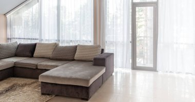 Büyük bir kanepe ve geniş pencereler. Pencerelerden sabah güneş ışığı