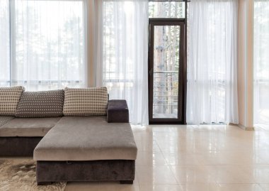 Büyük bir kanepe ve geniş pencereler. Pencerelerden sabah güneş ışığı