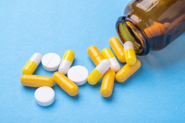 Mavi arka plandaki cam şişeden çok renkli haplar ve haplar.