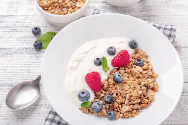 Fırında tahıllı yoğurt ve ahşap zemin üzerinde beyaz seramik tabakta böğürtlen. Sağlıklı kahvaltı.