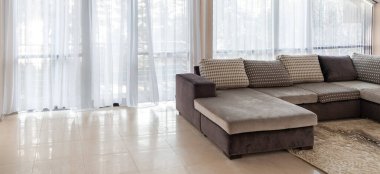 Büyük bir kanepe ve geniş pencereler. Pencerelerden sabah güneş ışığı