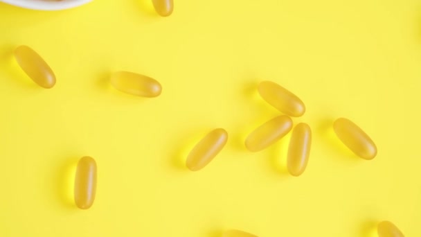 Vitamina D e Omega 3 cápsulas de óleo de peixe suplemento em uma placa em forma de coração sobre fundo amarelo. Conceito de saúde. Vista superior — Vídeo de Stock