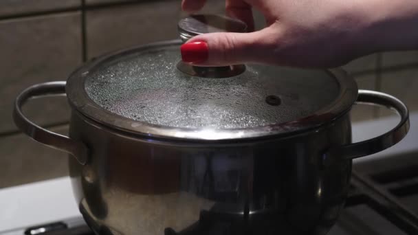 Mano hembra abriendo la tapa de vidrio de la bandeja de acero con agua hirviendo. Enfoque selectivo — Vídeos de Stock