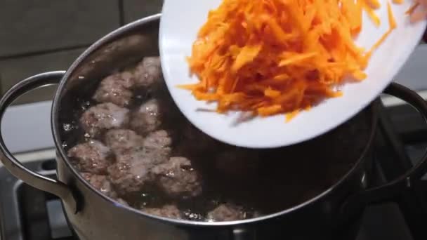 Umieszczenie marchewki w bulionie z klopsikami. Przygotowanie zupy klopsikowej. Zbliżenie. Skupienie selektywne — Wideo stockowe
