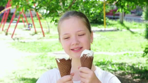 Porträt Teenager-Mädchen beim Eis essen lächelnd aus nächster Nähe. Glückliches Kind, das leckeres Eis im Freien isst. Mädchen blickt in die Kamera und lächelt. Sonniger Sommertag. Zeitlupe — Stockvideo