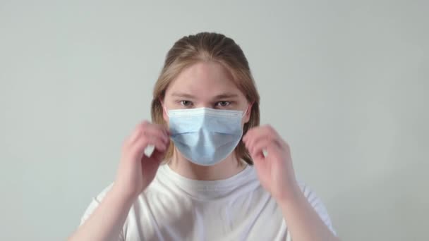 Portret van een jonge blanke jongeman doet een medisch masker af. Jongeman die naar de camera kijkt en lacht. Langzame beweging — Stockvideo