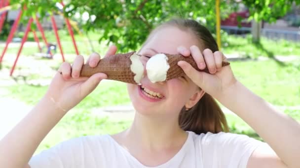 Retrato adolescente comiendo helado sonriendo de cerca. Niño feliz comiendo delicioso helado al aire libre. La chica mira a la cámara y sonríe. Día soleado de verano. Movimiento lento — Vídeos de Stock