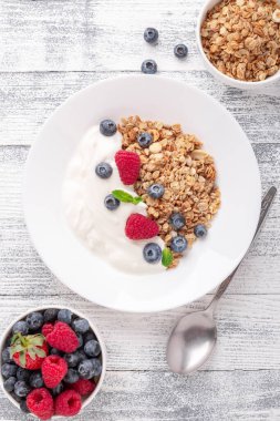 Yoğurtlu ev yapımı granola ve ahşap zemin üzerinde beyaz seramik tabakta taze böğürtlen. Dikey fotoğraf