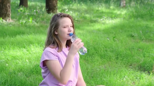 10代の少女は夏の公園でボトルから水を飲む。熱概念における飲料水 — ストック動画