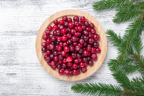 Raw fresh cranberries in wooden bowl and fir branches on light wood background. Top view. Copy space — Stock Photo, Image