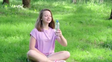 Yaz parkında şişeden su içen genç kız. Sıcaklık kavramında su içmek