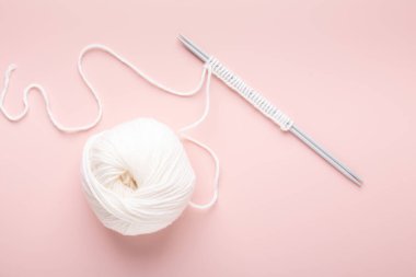 Beyaz örgü yünü ve pastel pembe arka planda örgü iğneleri. Hobi örgü. Üst görünüm