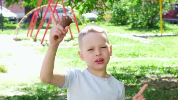 Portré kisfiú jégkrémet eszik, közelről mosolyogva. Boldog gyermek eszik finom fagylaltot a szabadban. A fiú a kamerába néz és mosolyog. Napfényes nyári nap. Lassú mozgás. — Stock videók