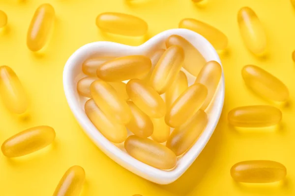 Η βιταμίνη D και το ωμέγα 3 κάψουλες ιχθυελαίου συμπληρώνουν σε μια πλάκα σχήματος καρδιάς σε κίτρινο φόντο. Έννοια της υγειονομικής περίθαλψης. Άνω όψη — Φωτογραφία Αρχείου