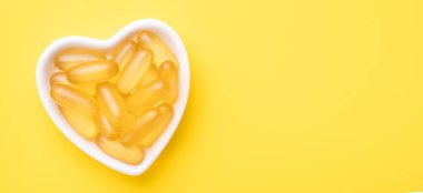 Sarı arka planda kalp şeklinde bir tabakta Omega 3 kapsüllü yatay pankart. Balık yağı softgelleri. Pankart. Boşluğu kopyala