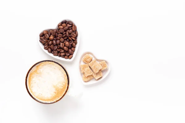 Taza de café y platos en forma de corazón con granos de café y azúcar morena sobre fondo blanco. Vista superior. Copiar espacio — Foto de Stock