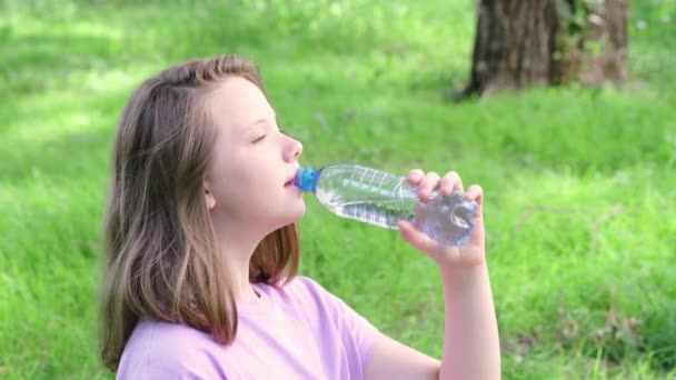 Tonårstjej dricker vatten från flaska i sommarparken. Dricksvatten i värmekonceptet. Närbild — Stockvideo