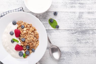 Fırında tahıllı yoğurt ve ahşap zemin üzerinde beyaz seramik tabakta böğürtlen. Sağlıklı kahvaltı. Boşluğu kopyala