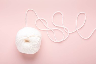 Pastel pembe arka planda beyaz örgü yünü. Hobi örgü. Üst görünüm
